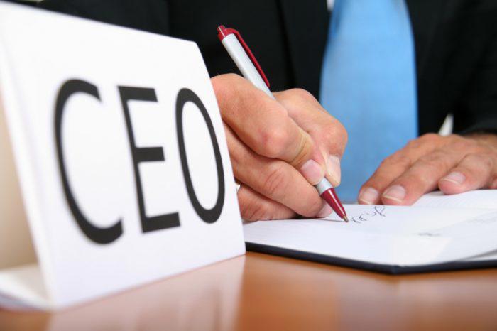 Person writing on a piece of paper with CEO card on desk