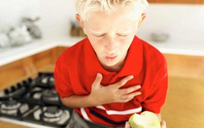 Blonde boy child clutching chest in pain holding a pear